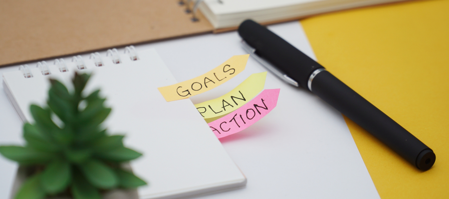 A desk with a notebook, sticky notes reading 'Goals, Plan, Action,' and a pen, symbolizing practical tools for leadership development.