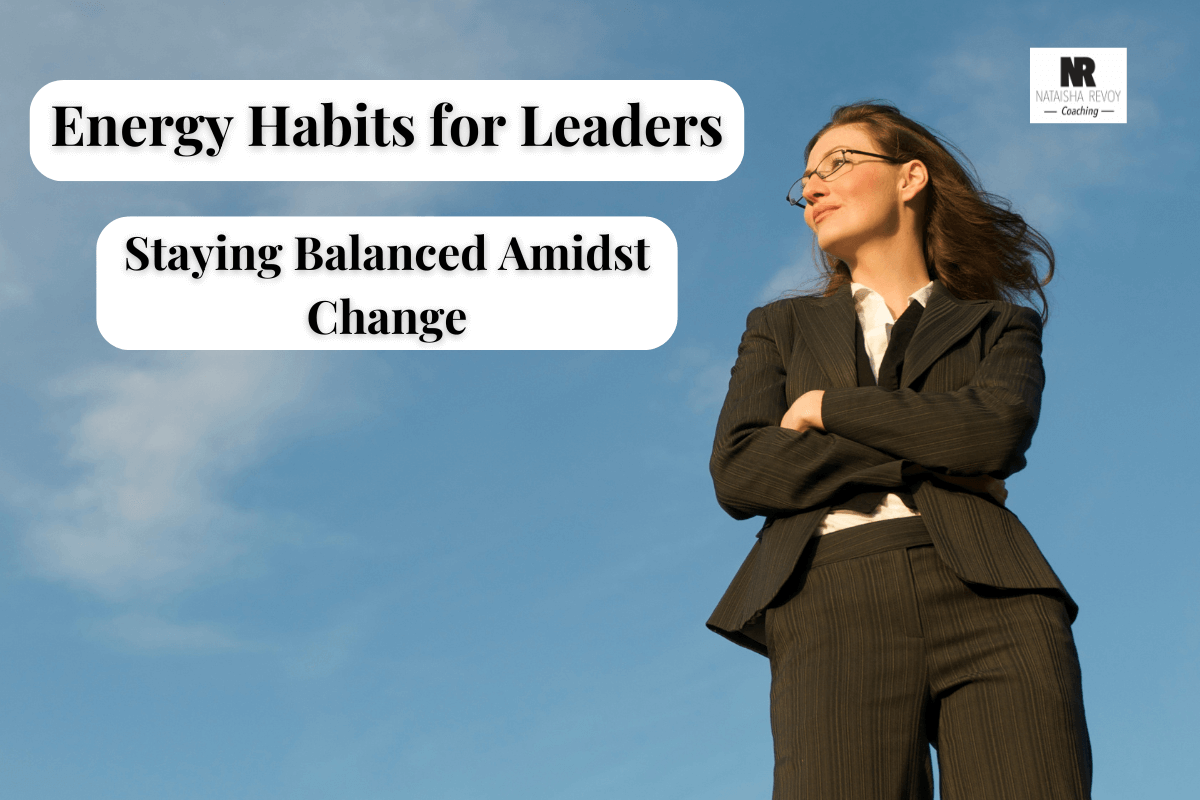 Confident businesswoman in a suit standing outdoors under a clear blue sky with text overlay: ‘Energy Habits for Leaders – Staying Balanced Amidst Change.’